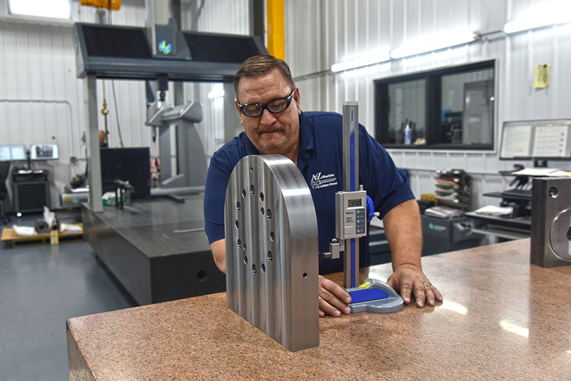 An A to Z Machine employee quality a checking a custom made part sitting on a table