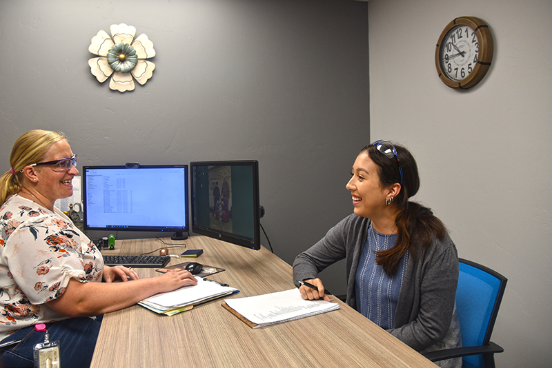 Two women smiling and collaborating at a desk in an office