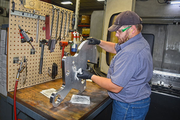 an A to Z Machine machinist polishing a custom metal part on a workbench