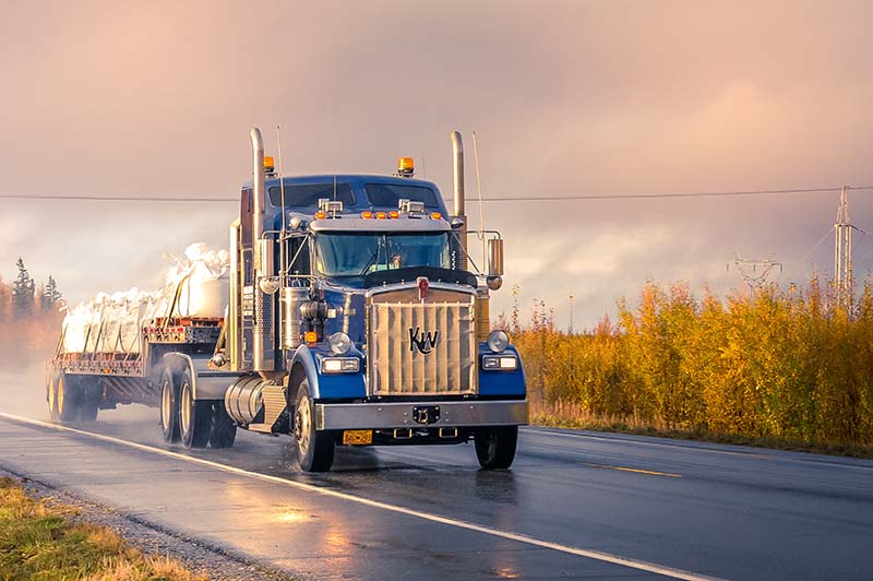 a large open bed semi driving down a two lane road