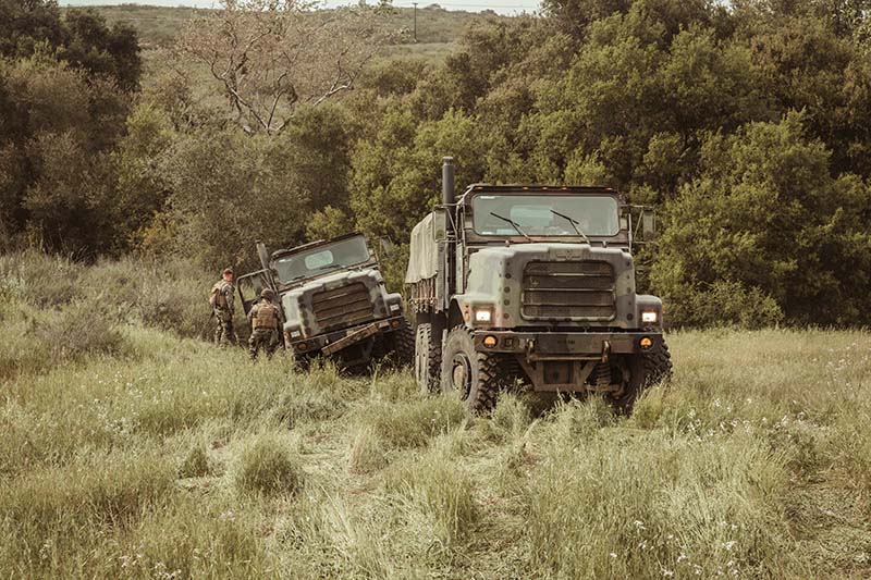 2 large military vehicles driving through an open field